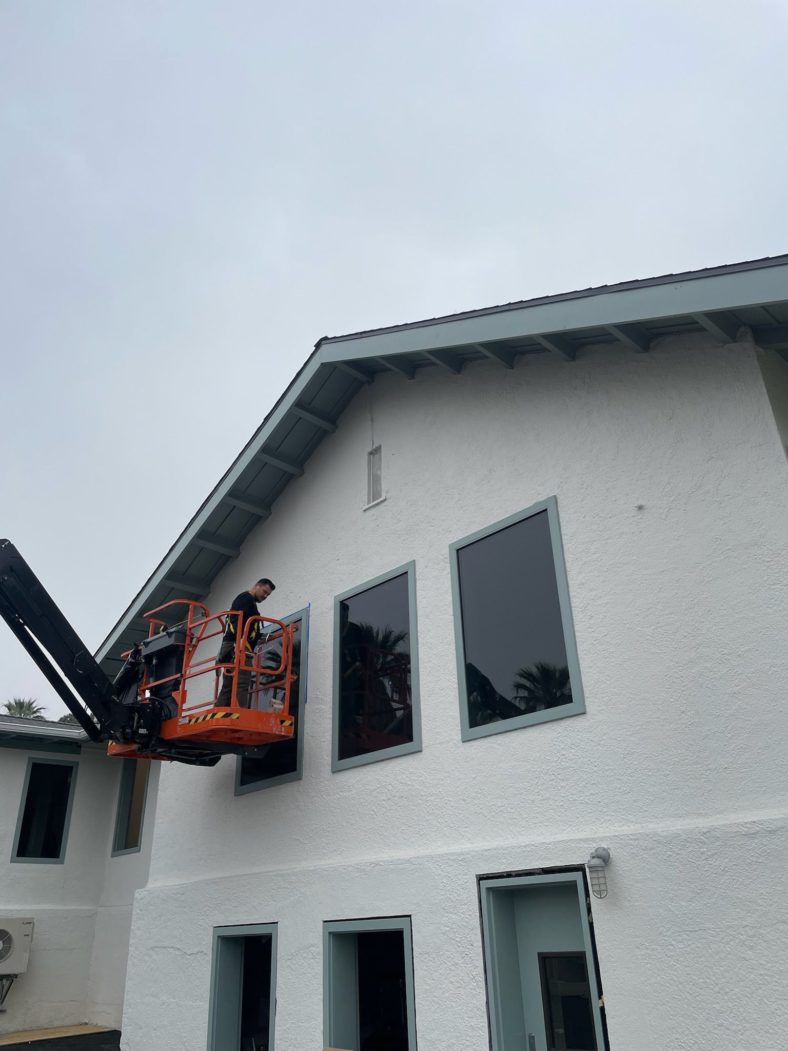 Person in an aerial lift working on windows of a white building with dark-tinted windows on a cloudy day.