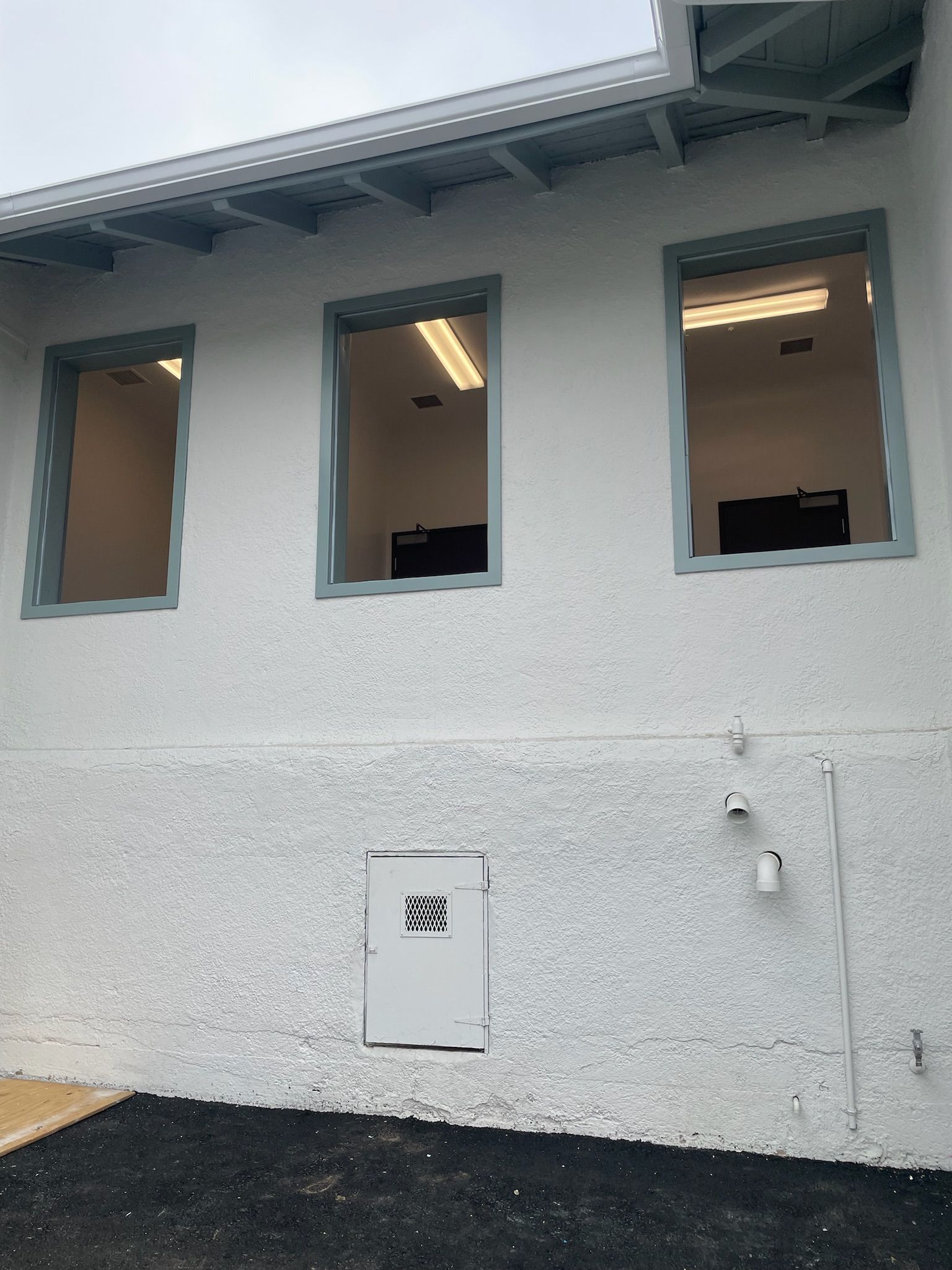 Exterior of building with three windows, white stucco walls, light blue trim, and a small door.