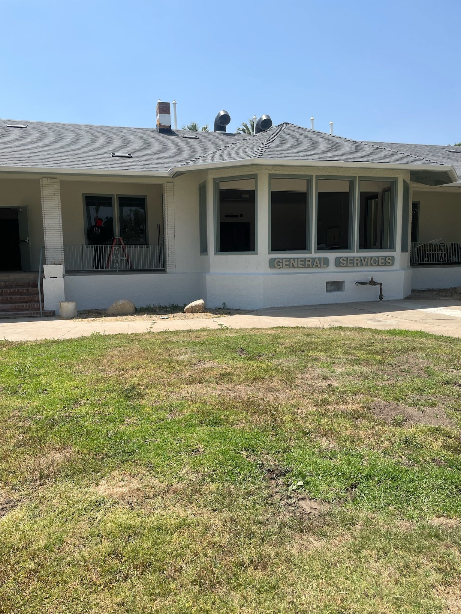 A one-story white building with a porch and windows under a blue sky, in a grassy area.
