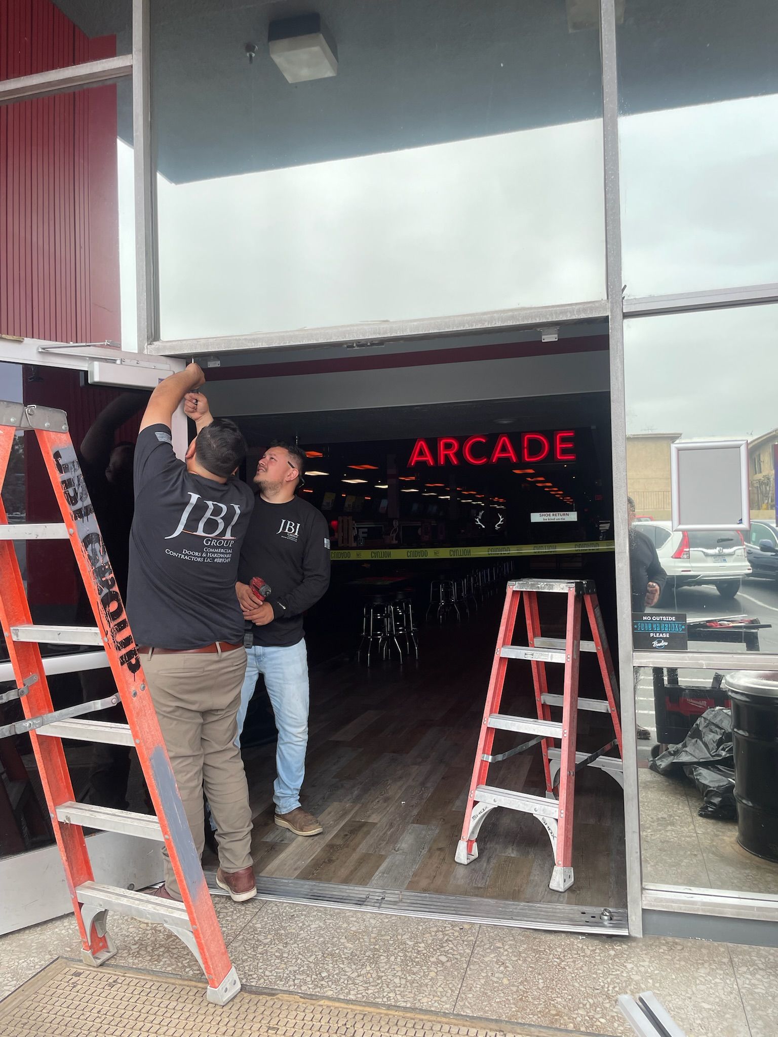 People installing glass door at an arcade. Ladders present. Arcade sign visible.