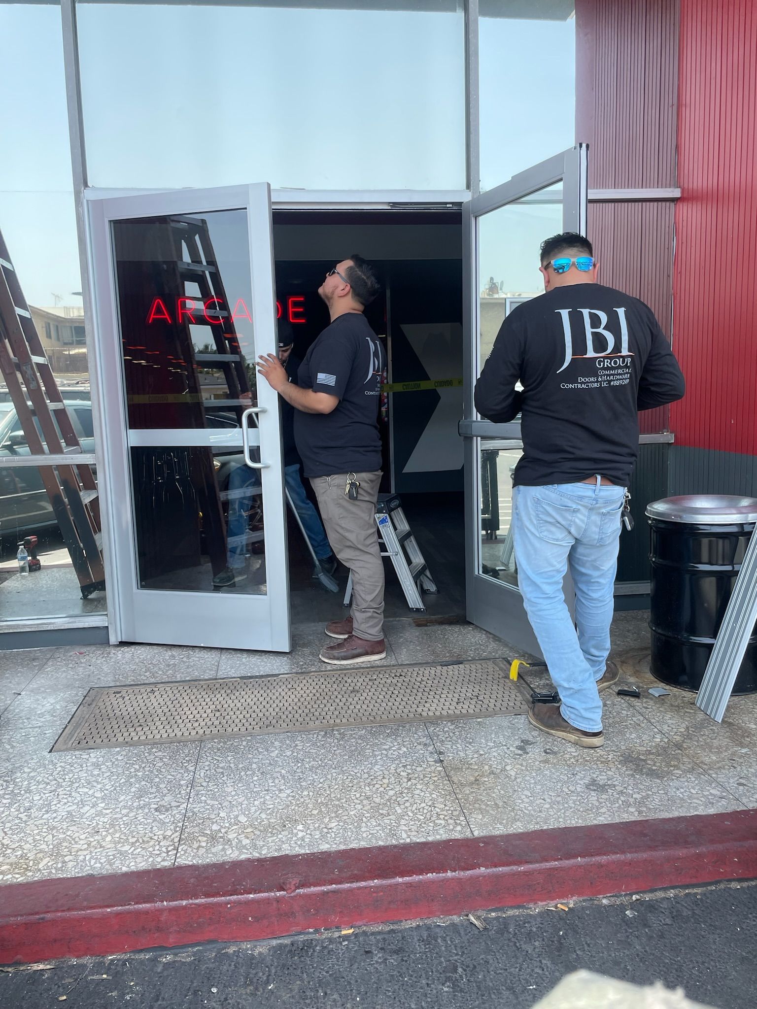 Two men installing a door. Building exterior with red accents. One man looks up at the door, another walks towards it.