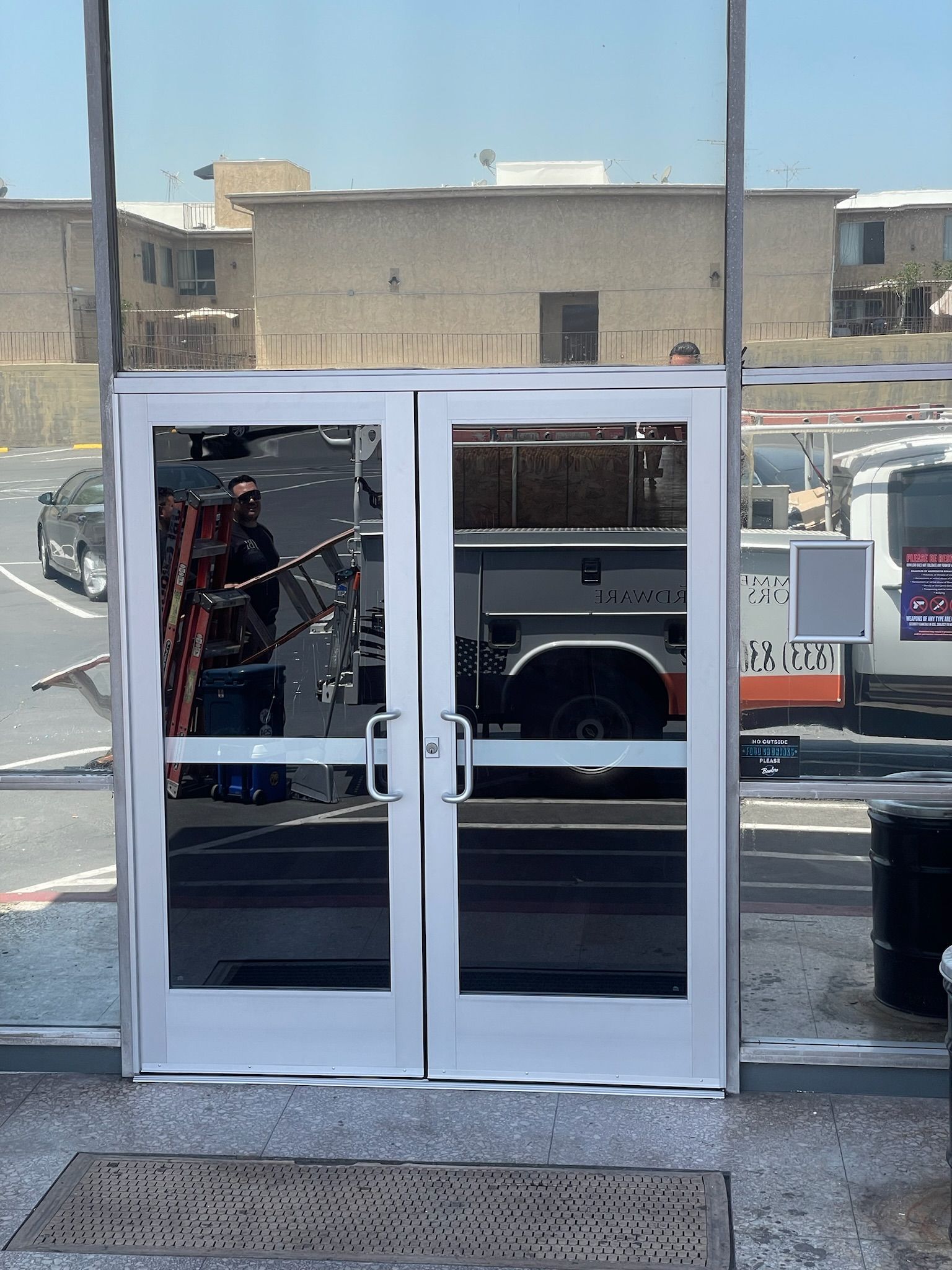 Glass doors in a building facade, reflecting parked vehicles and a ladder.