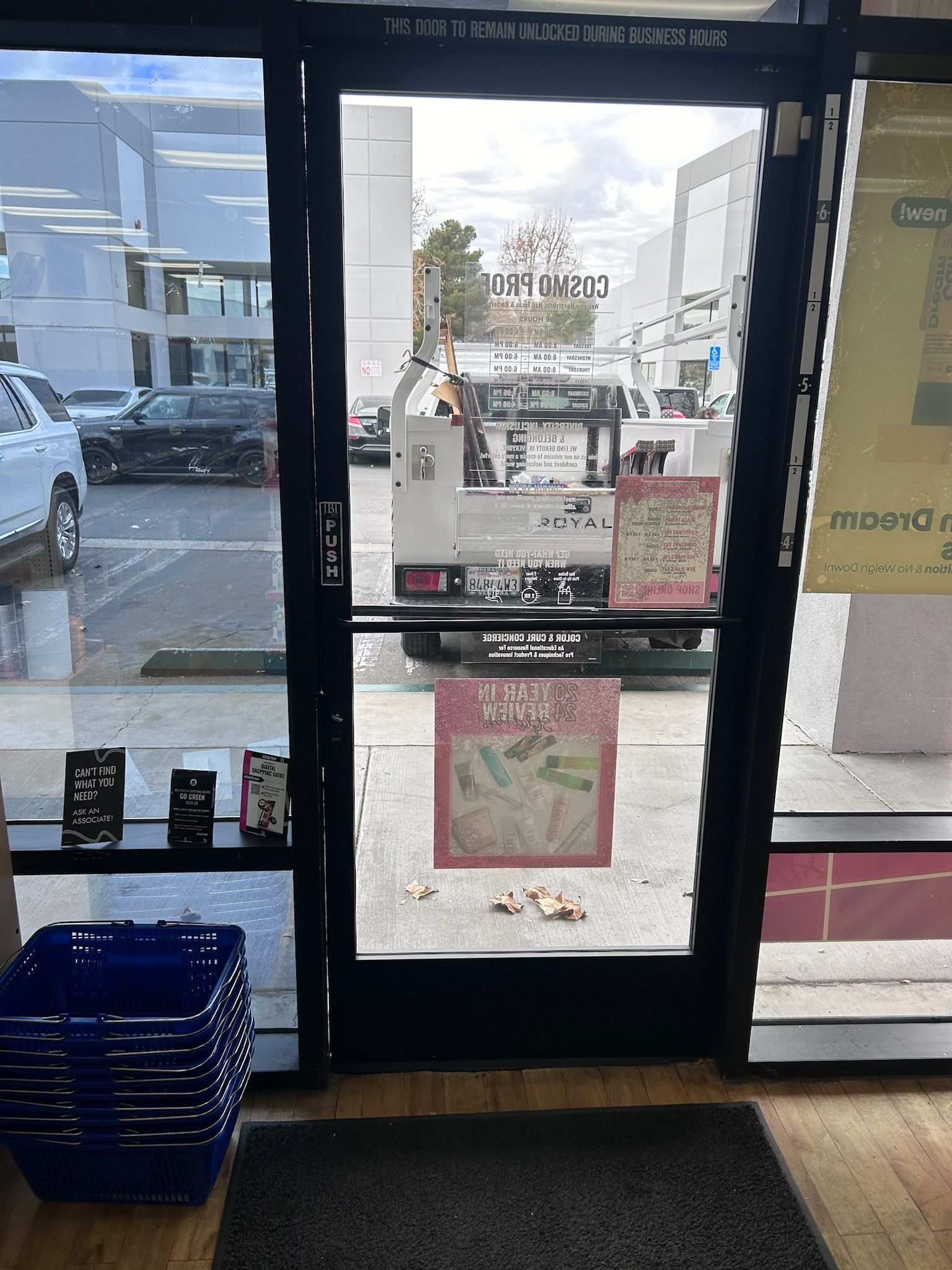 A store entrance with a glass door, revealing a street scene with a truck and parked cars.