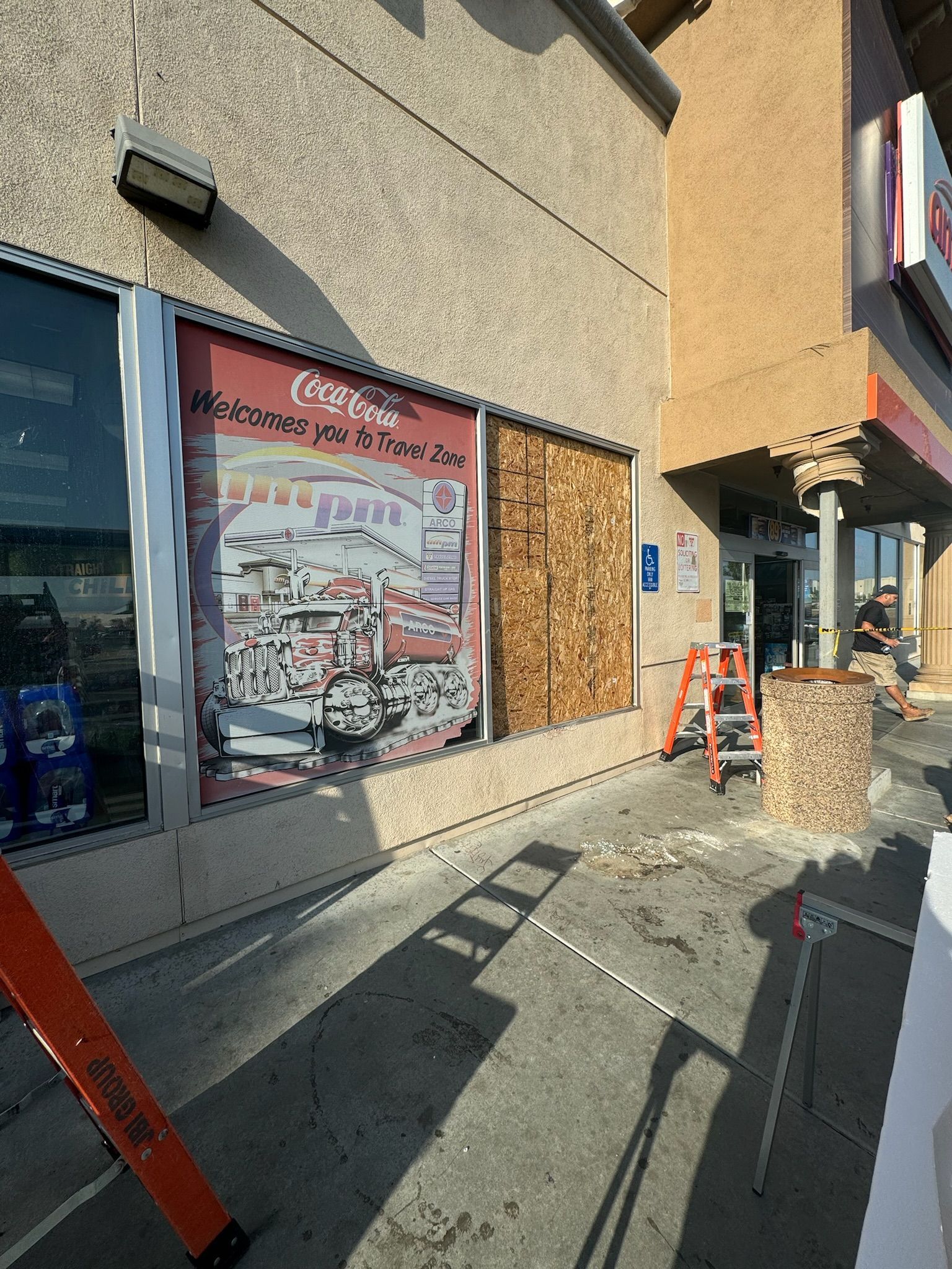 Building exterior with boarded-up window, a ladder, and a worker visible in the doorway.