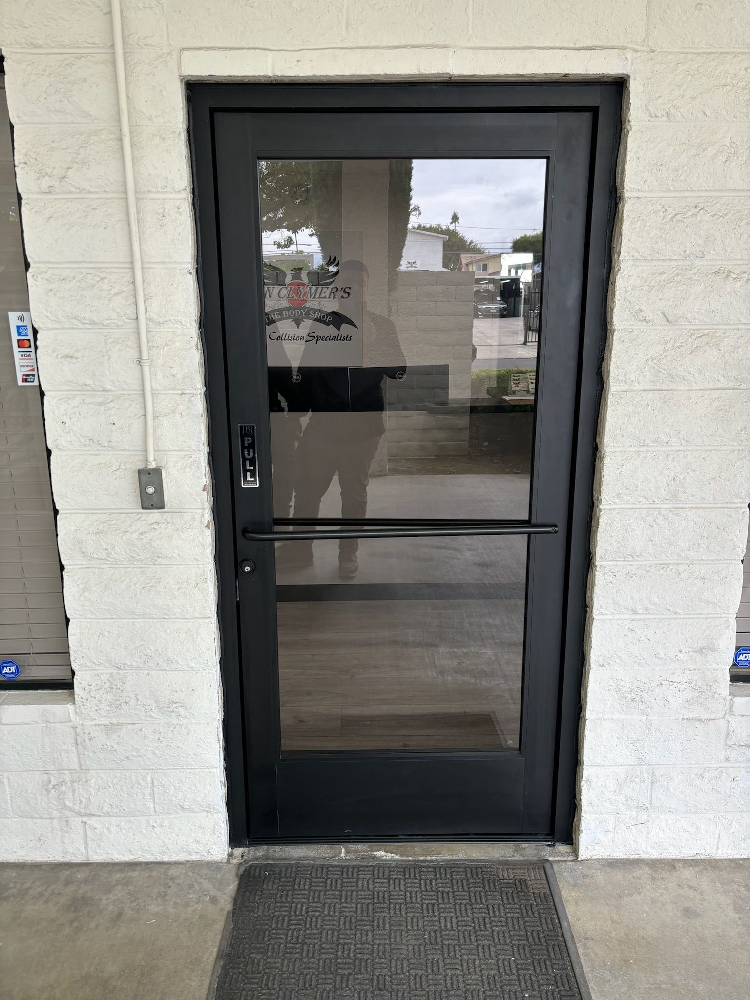 Black glass door with a horizontal bar, inside a white brick building.