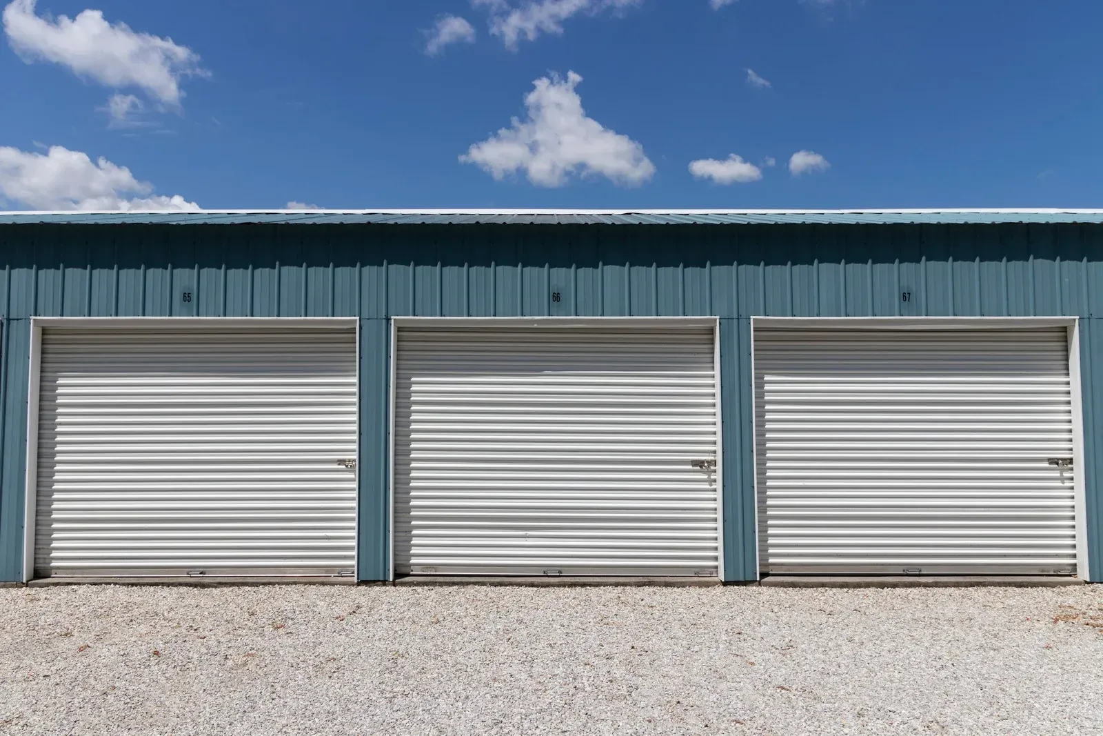 Three metal storage unit doors with a blue building against a partly cloudy sky.