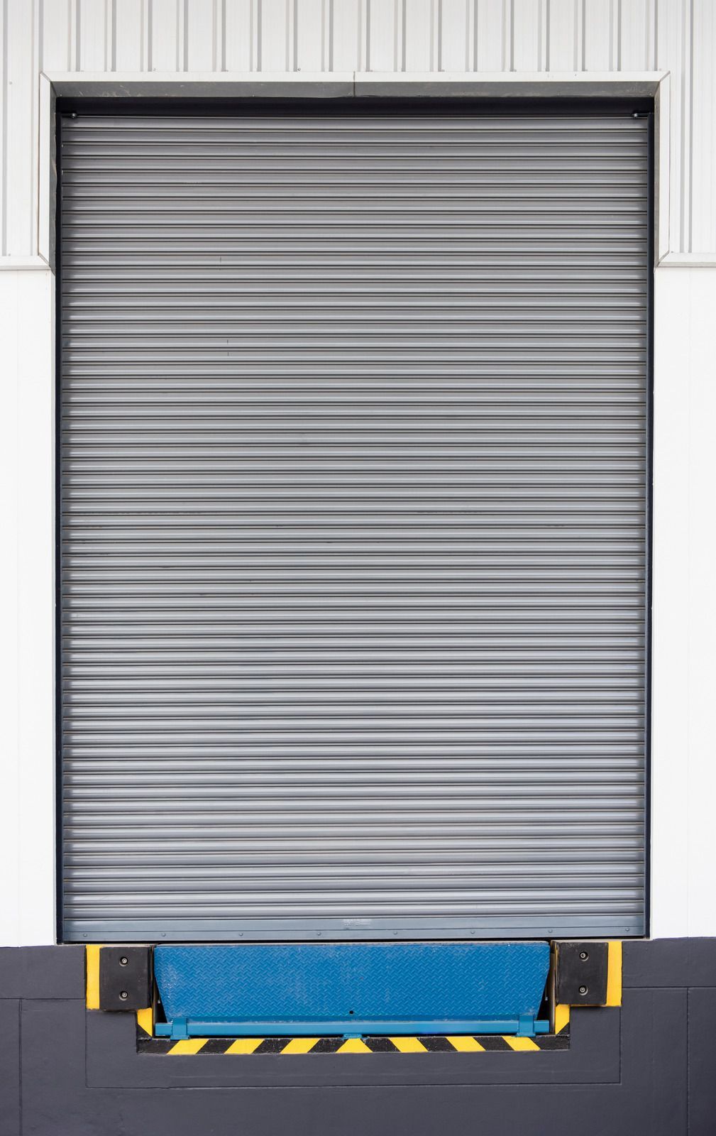 Closed gray industrial roll-up door on a loading dock with a blue bumper.