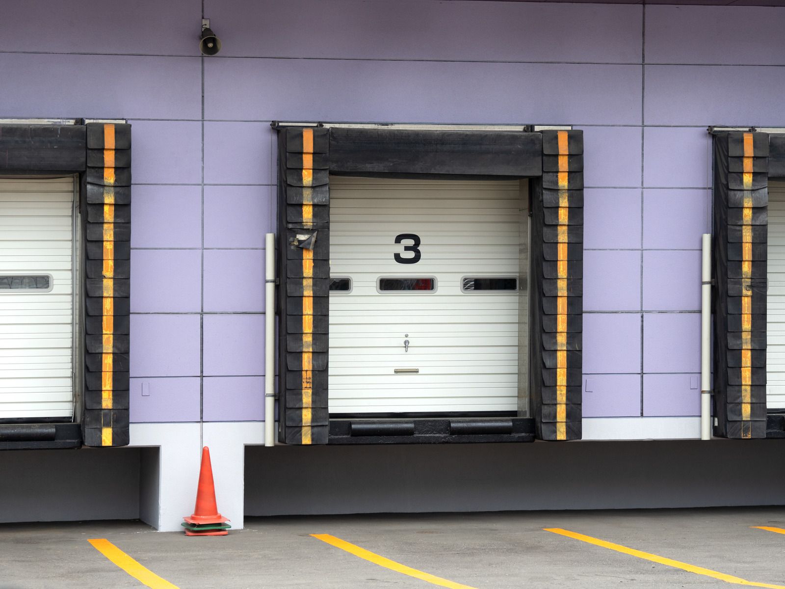 Loading dock doors, one open with number 3, on a purple building with parking lines.