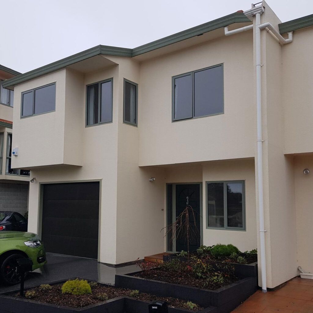 A white house with a green car parked in front of it.