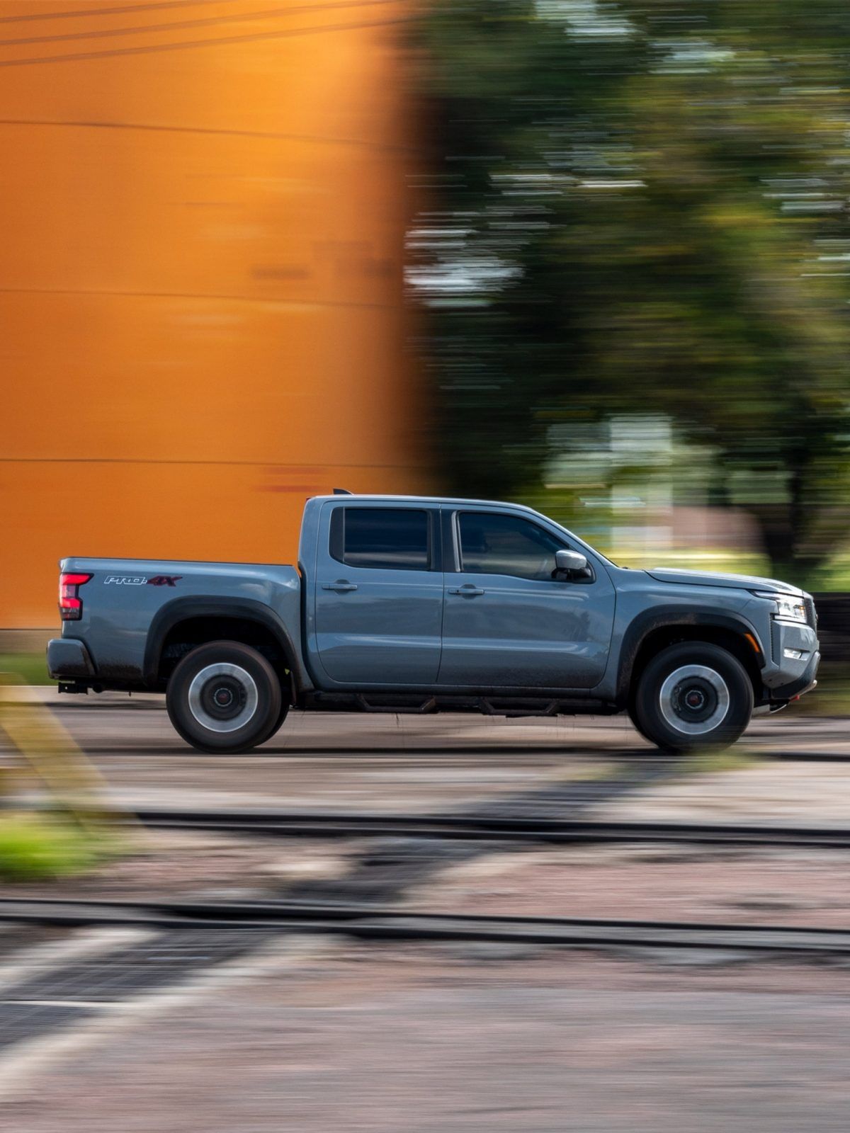 Camioneta gris pasando junto a una pared naranja con efecto de desenfoque de movimiento.