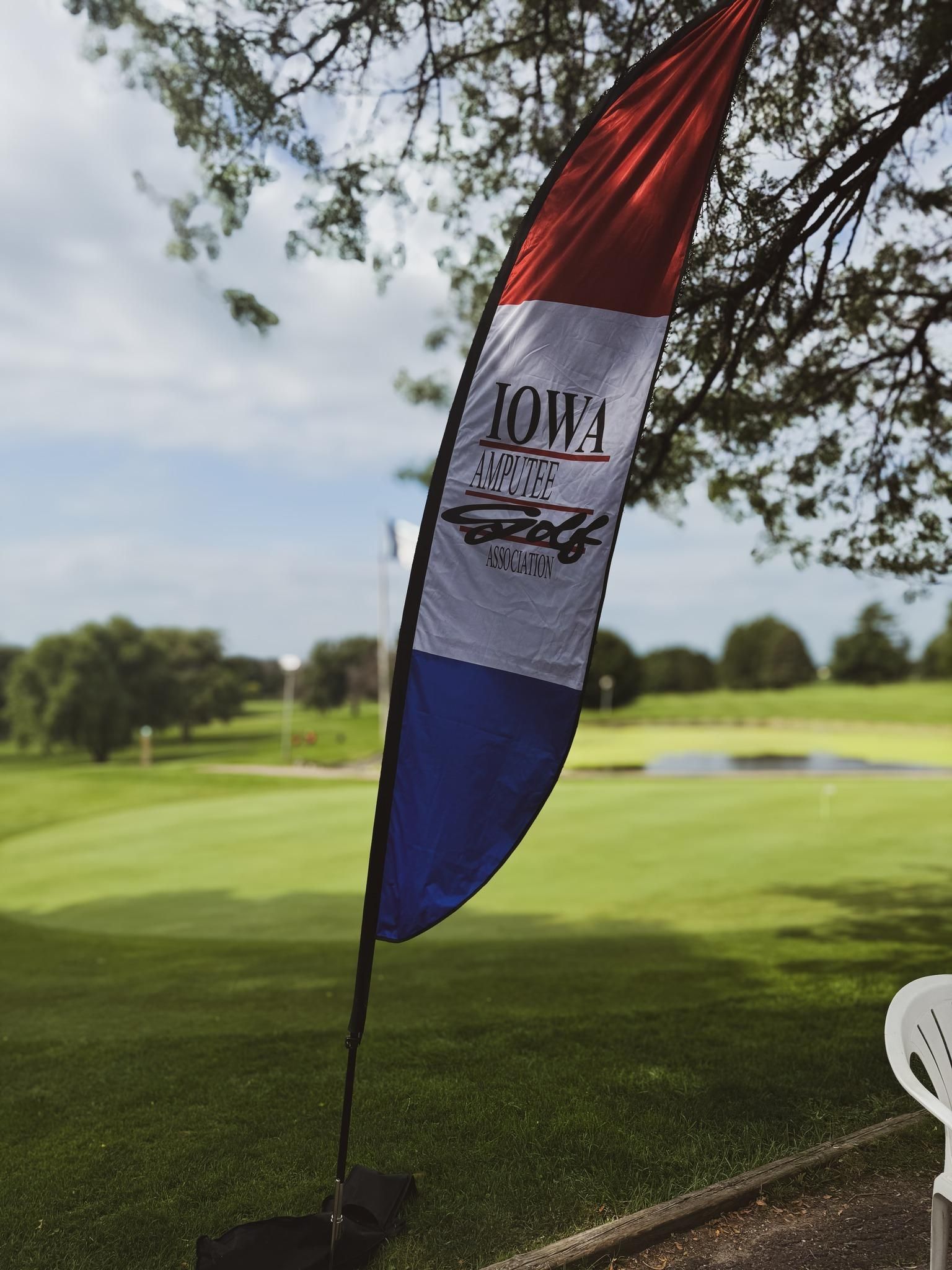 A red , white and blue flag is hanging from a tree in front of a golf course.