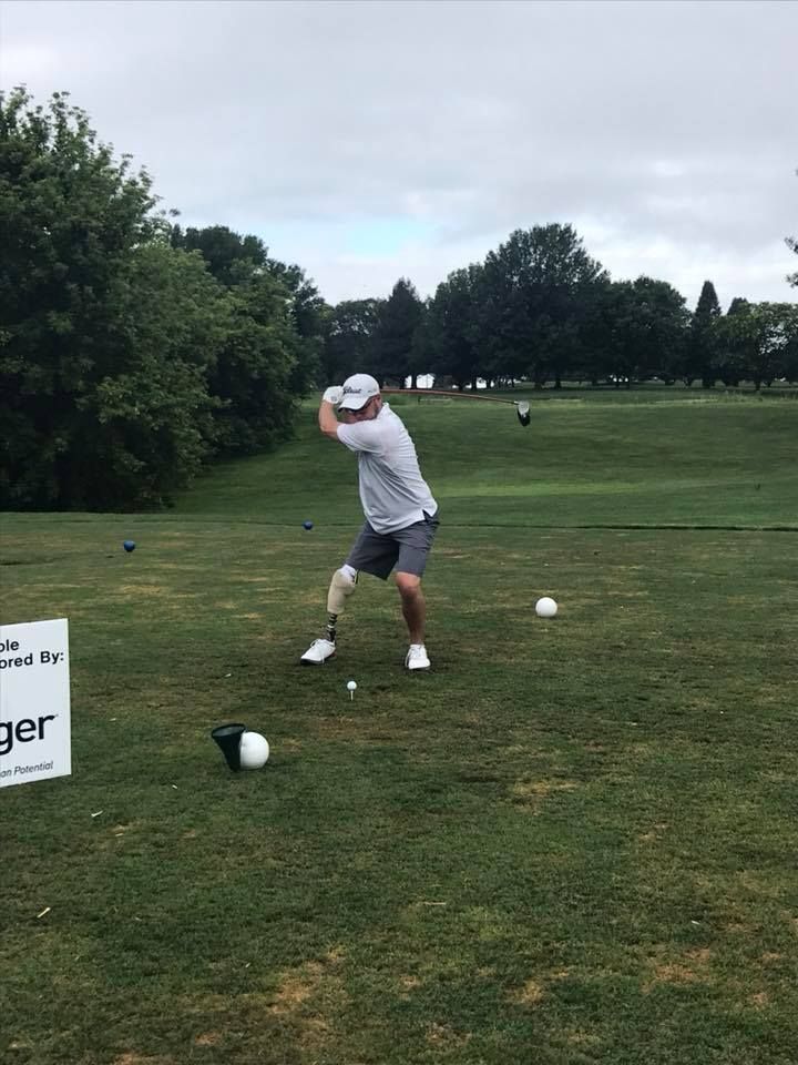 A man with a prosthetic leg is swinging a golf club on a golf course.