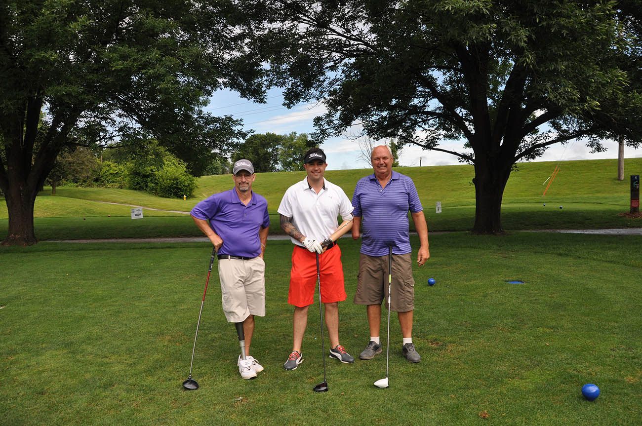 Three men are standing on a golf course holding golf clubs.
