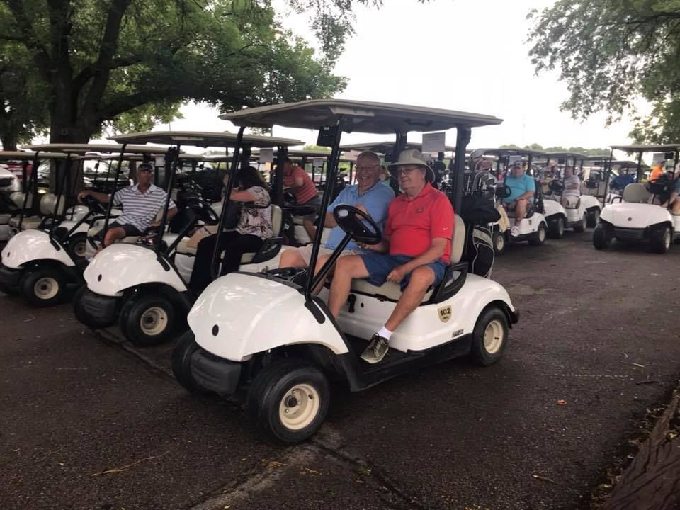 A group of golf carts are parked in a parking lot.