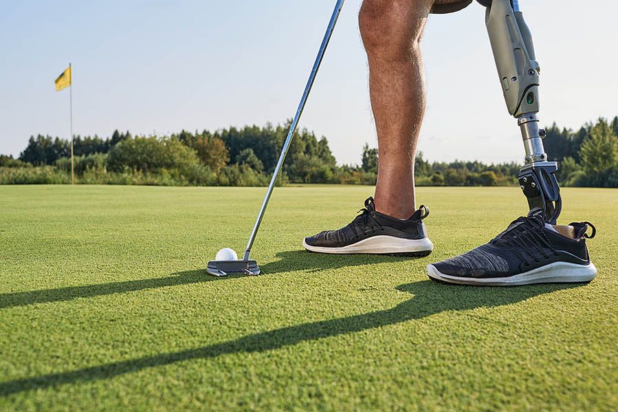 A man with a prosthetic leg is putting a golf ball on a golf course.