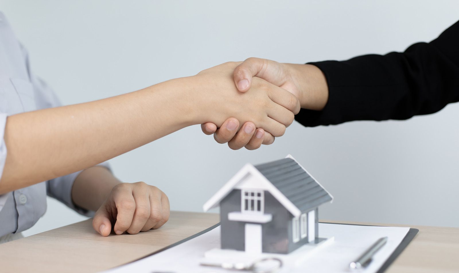 A woman is shaking hands with a real estate agent in front of a model house.