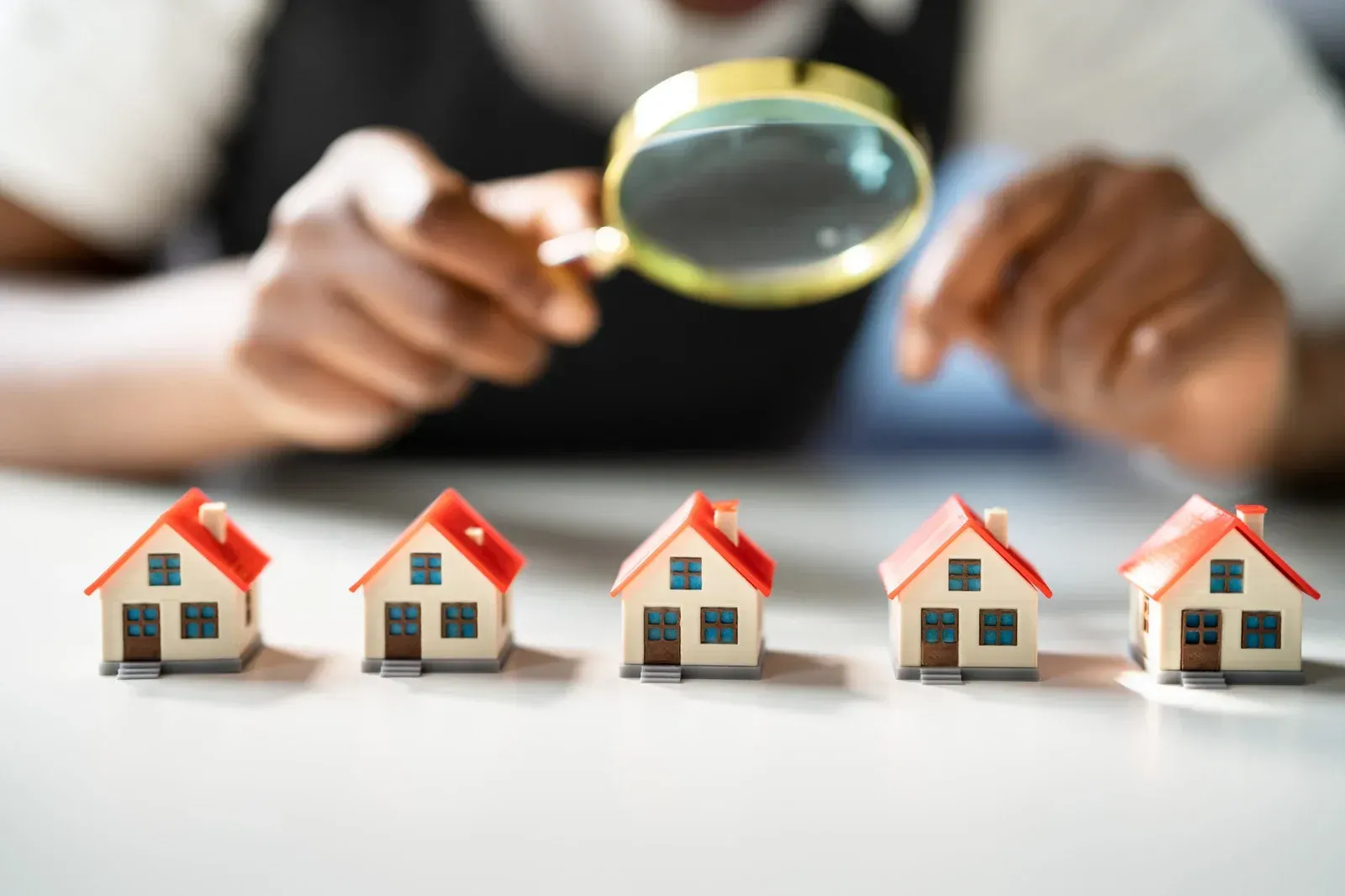 A person is looking through a magnifying glass at a row of small houses.
