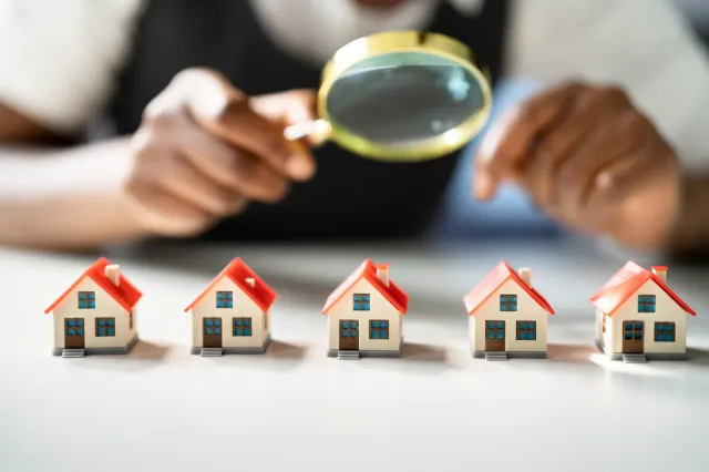A person is looking through a magnifying glass at a row of small houses.