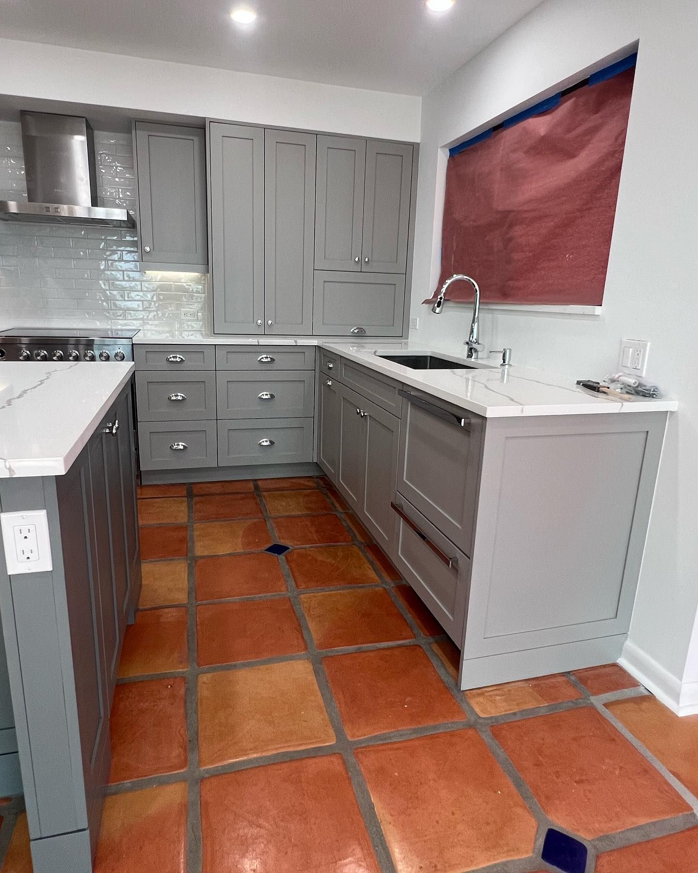 A kitchen with gray cabinets and red tile floors.