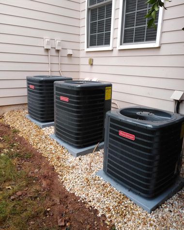 Three outdoor AC units beside a house wall on a bed of white gravel.