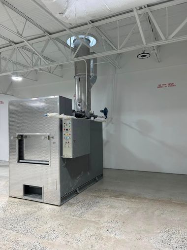 Industrial machine in a white showroom with a metallic enclosure and overhead ducting.