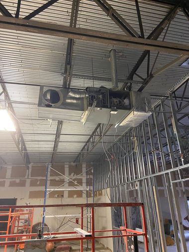 Construction site ceiling with suspended HVAC ducts, metal framing, and scaffolding under a corrugated roof.