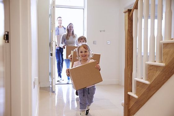 A family of four moves boxes into a house.