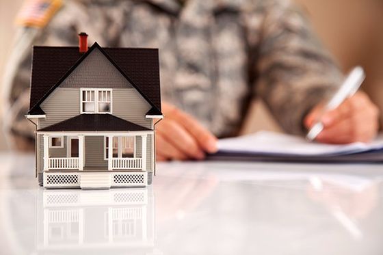A uniformed person signs papers with a model home in the foreground.