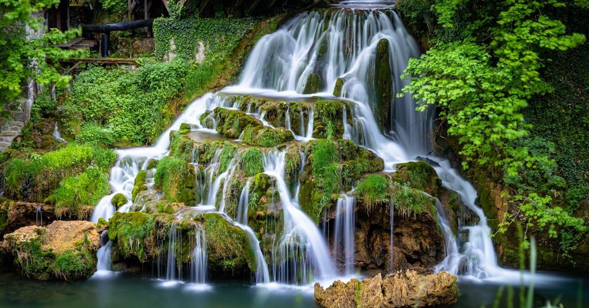 Waterfall cascading over mossy rocks into a pool, surrounded by lush green foliage.
