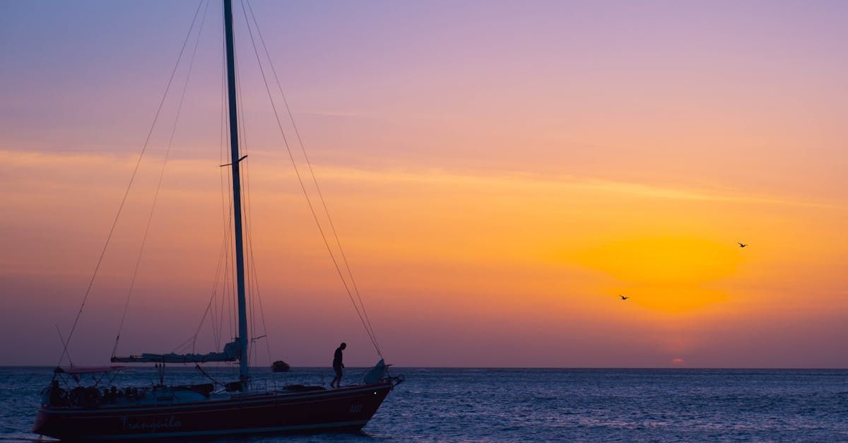 Sailboat at sunset with orange, purple and blue sky over the ocean.