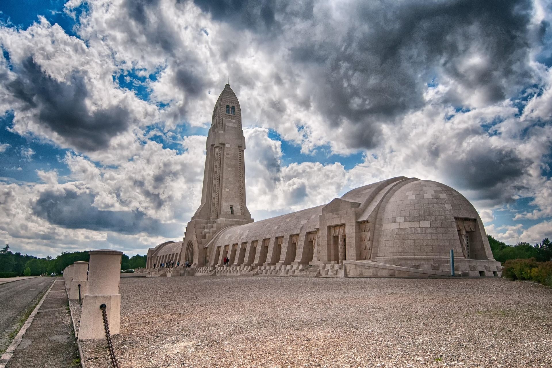 Monument to the fallen in Verdun, France, a tall tower with an arched structure below, under a cloudy sky.