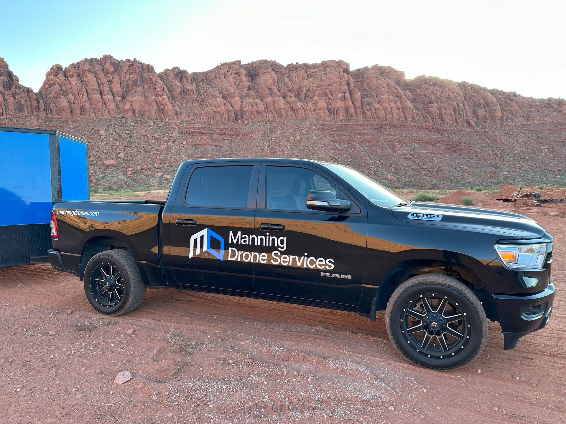 A black ram truck is parked next to a blue trailer.