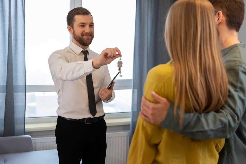 An agent hands keys to a smiling couple in a bright room, symbolizing a successful home purchase.