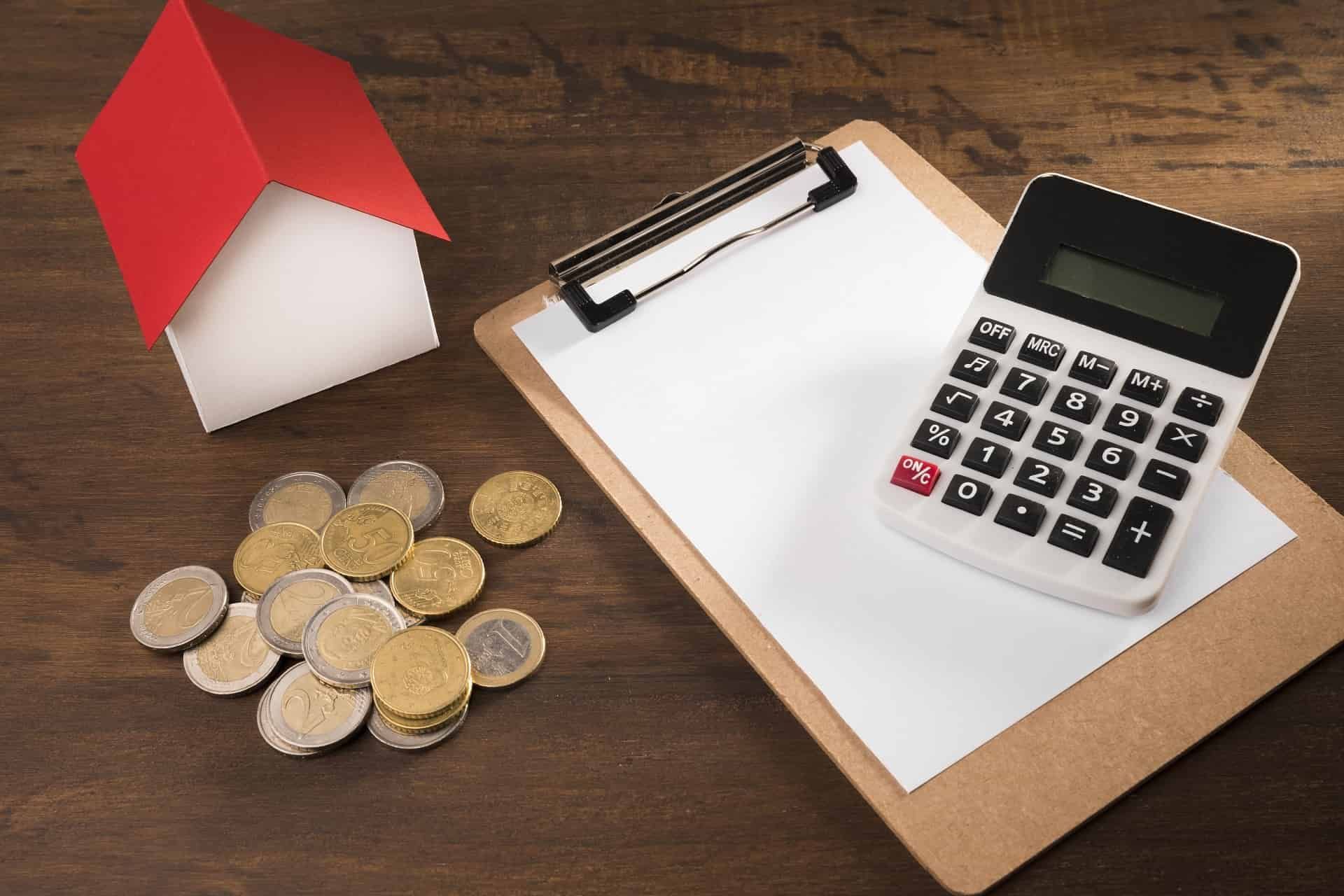 A toy house, Euro coins, a clipboard, and a calculator on a table suggest real estate and finance themes.