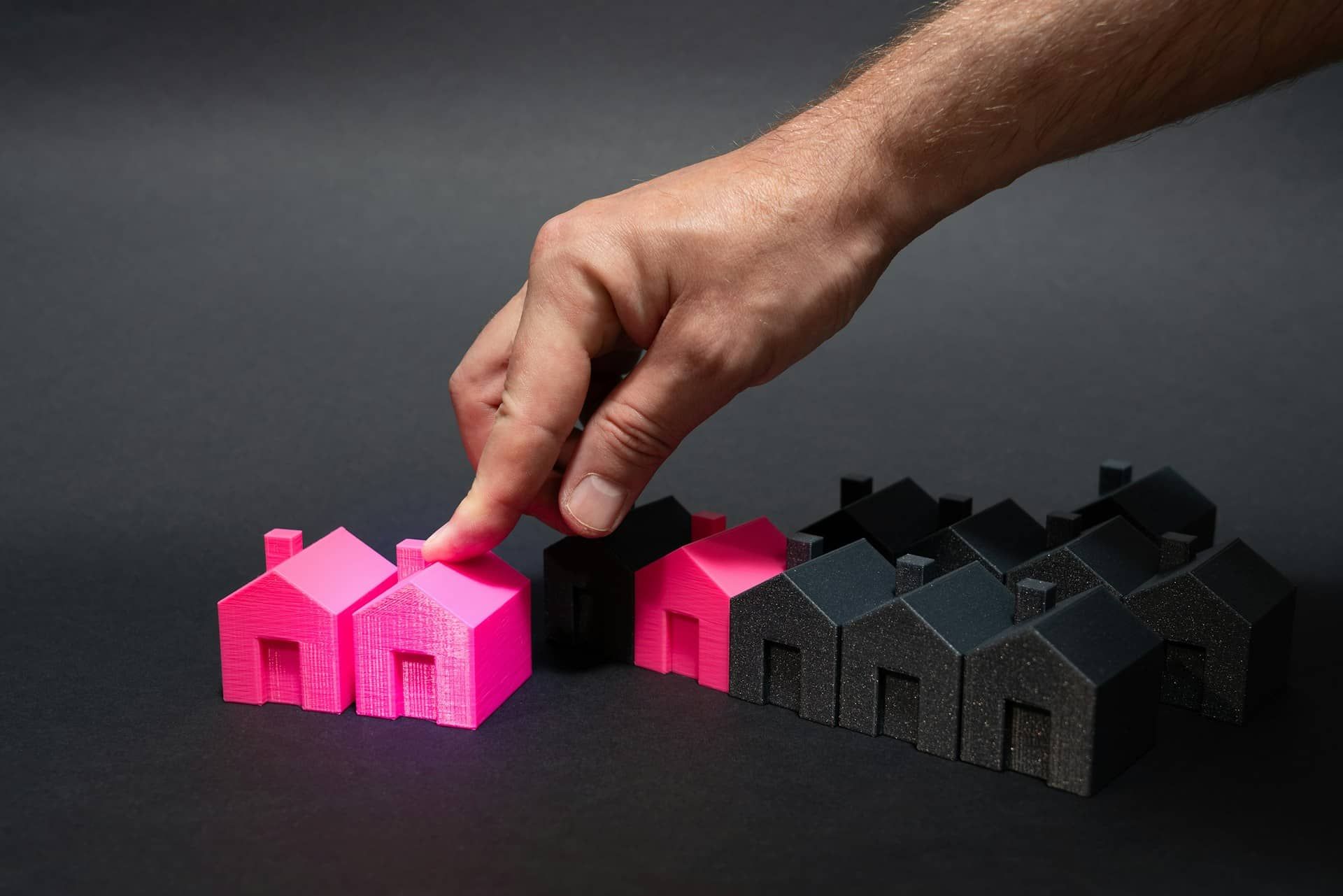 A hand adjusts a pink house among others, symbolizing choice and standing out from the crowd.