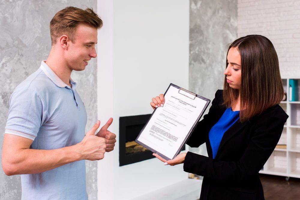 In an office, a man in a blue shirt gives a thumbs-up to a woman in a blazer holding a clipboard, creating a positive vibe.