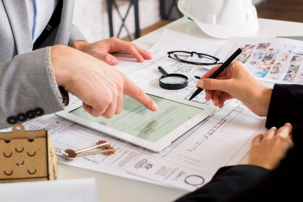 Two professionals review plans on a tablet, surrounded by documents and tools, showing collaboration and focus.
