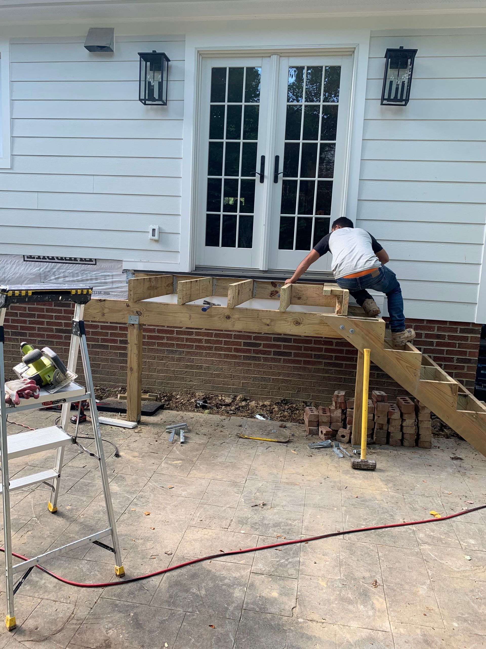 A person builds wooden steps leading to a white door. The building has a brick base.