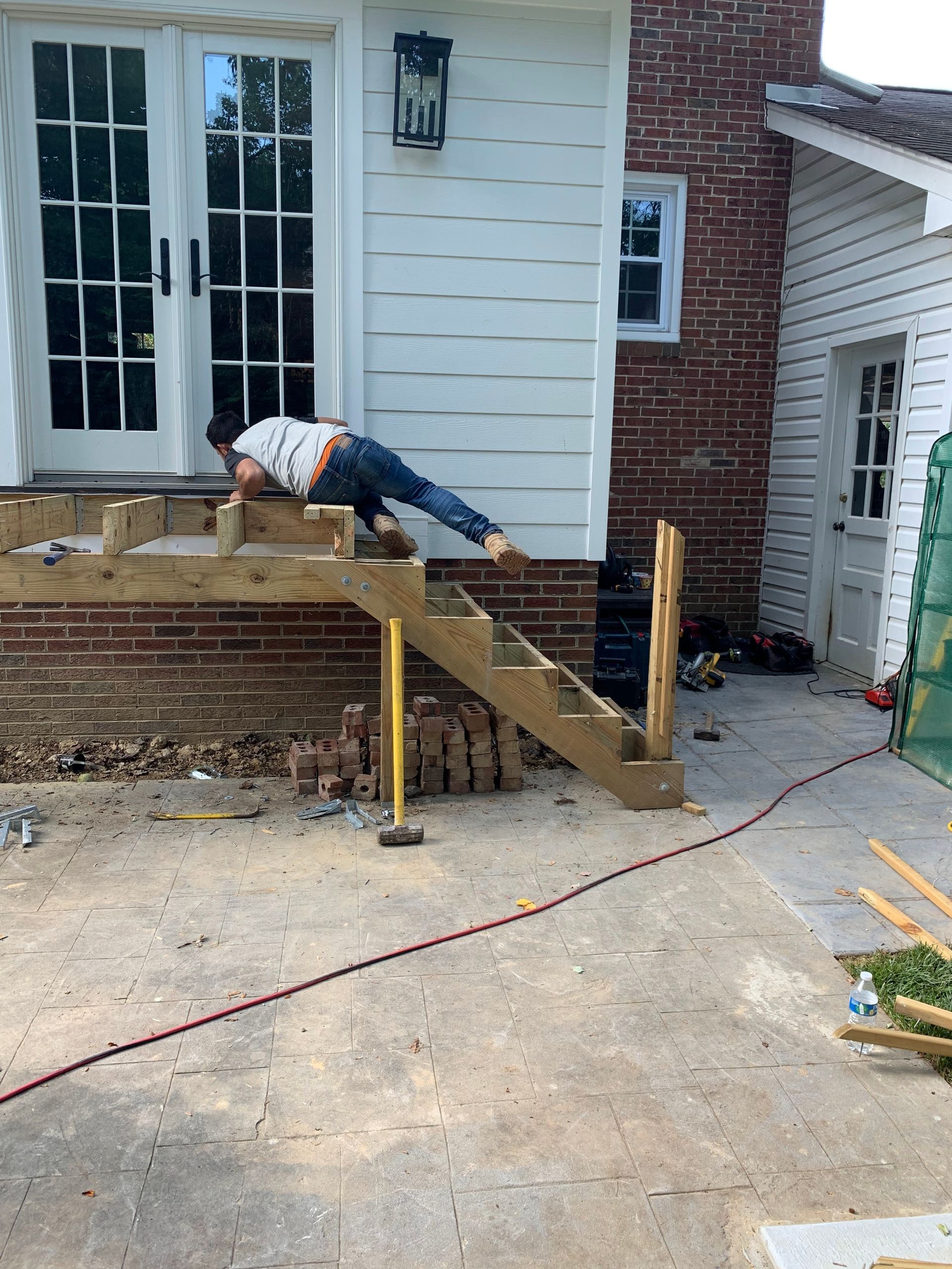 Person building wooden stairs attached to a house. Exterior setting with brick and white siding.
