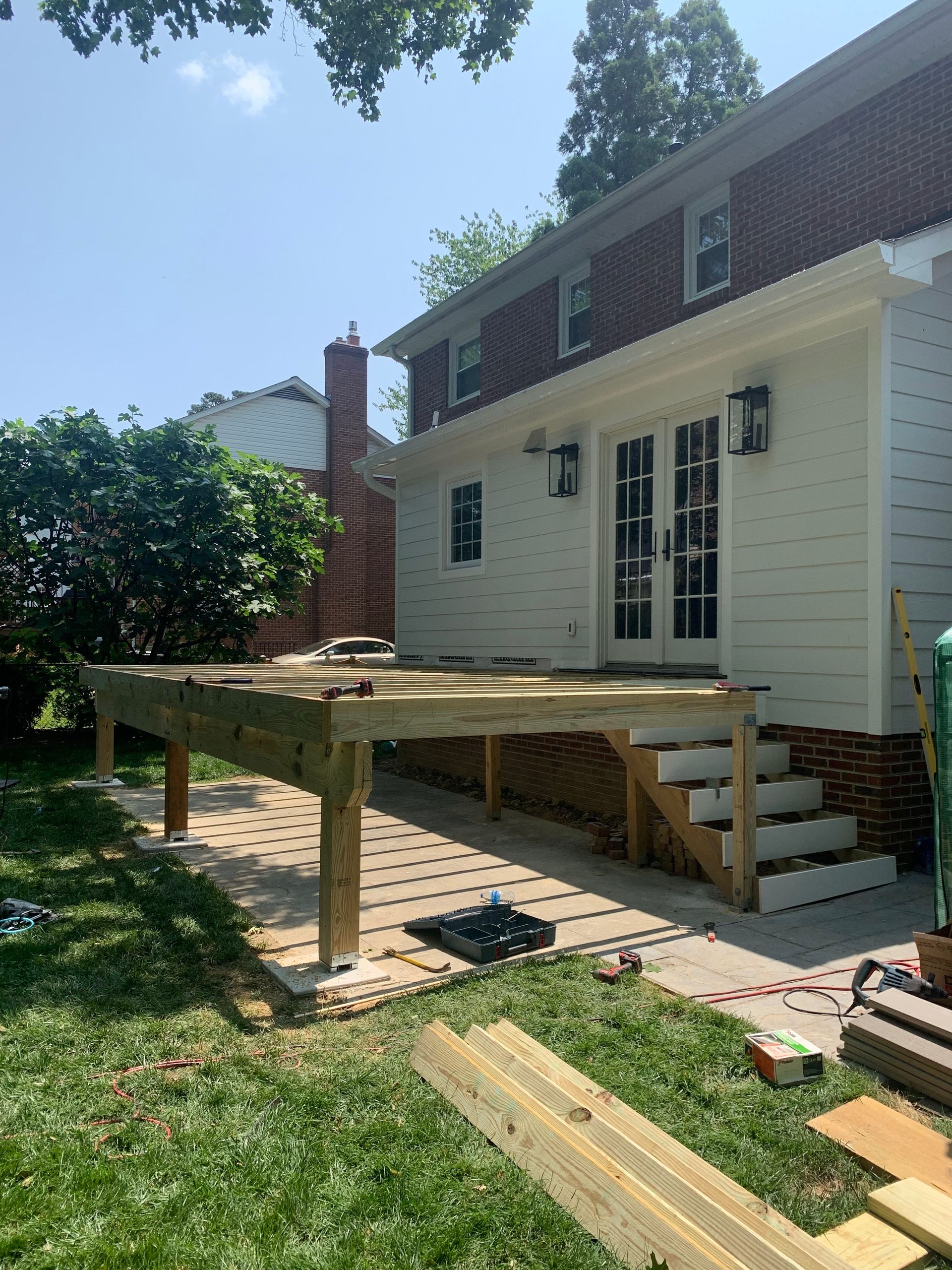 A wooden deck under construction next to a two-story brick and white-sided house with steps.