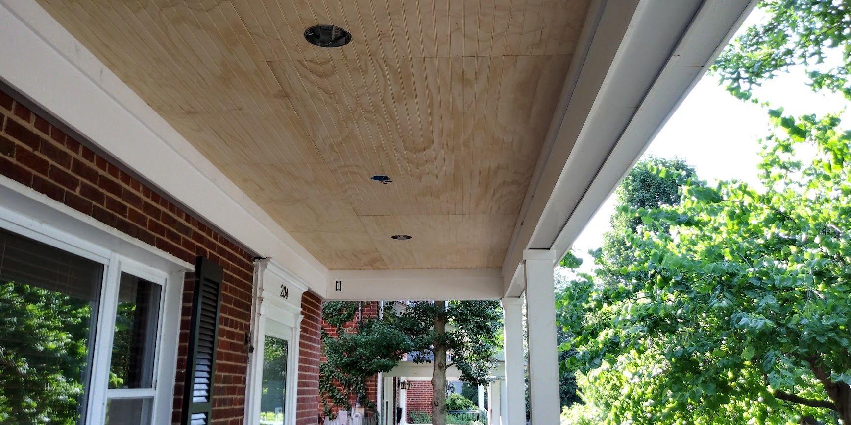 A porch ceiling with light fixtures. The ceiling is made of wood and is above a brick building.