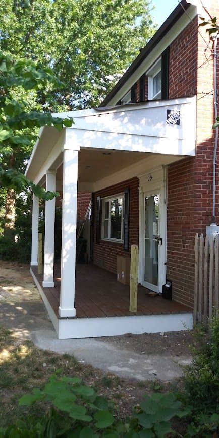 Porch of a brick house with white columns and a door. Brown deck and concrete pathway.