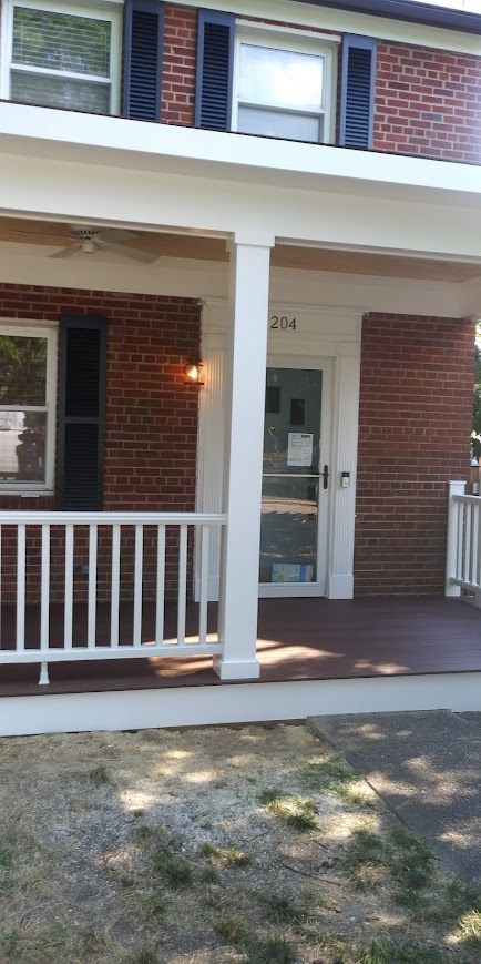 Brick building with a porch, white railing, and a door with a sign.