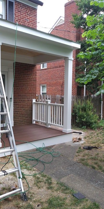 A house with a porch. A ladder is leaning against the house. There is a hose on the ground.