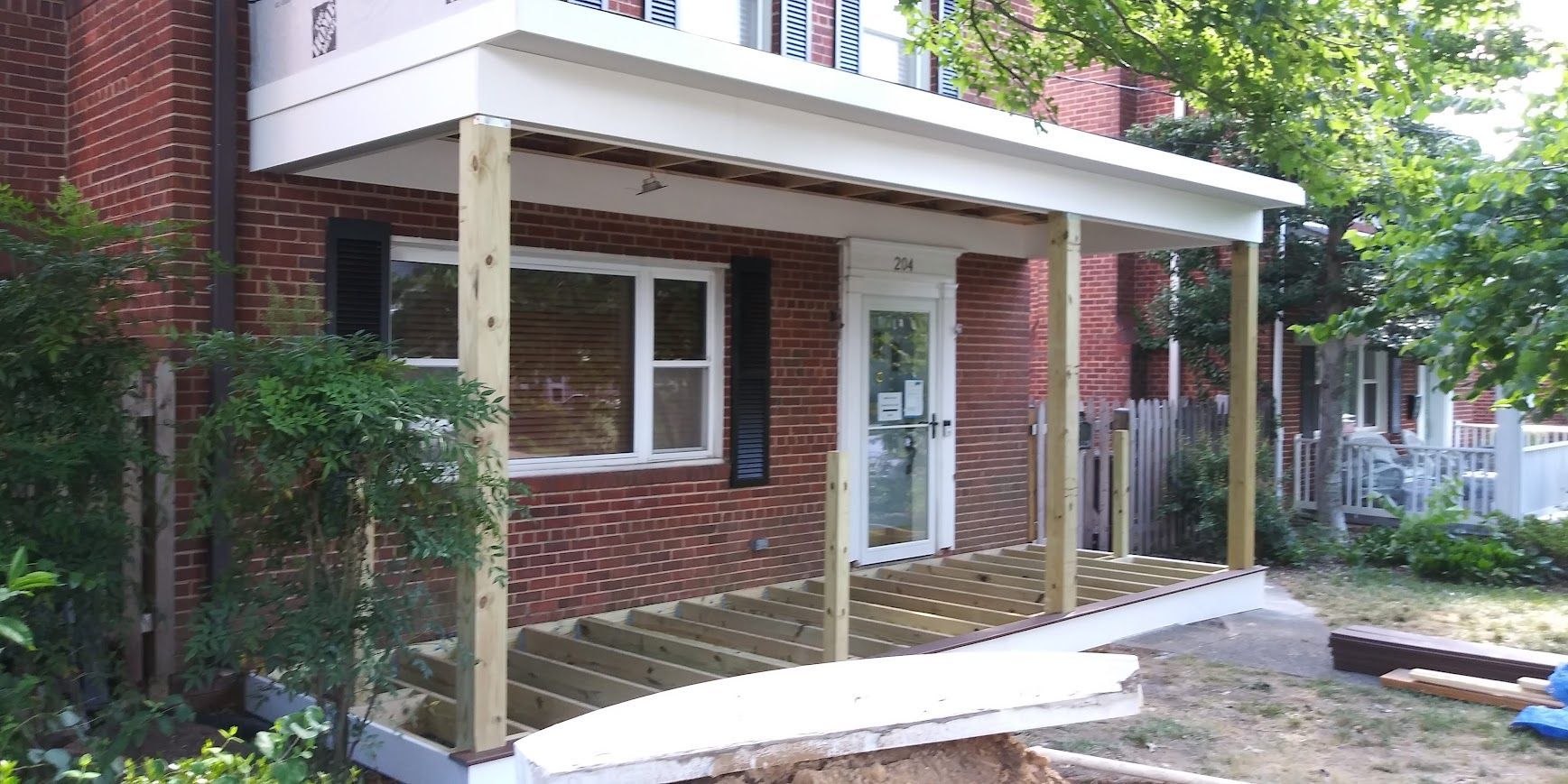 A porch is under construction on a brick building with a white roof and wooden supports.