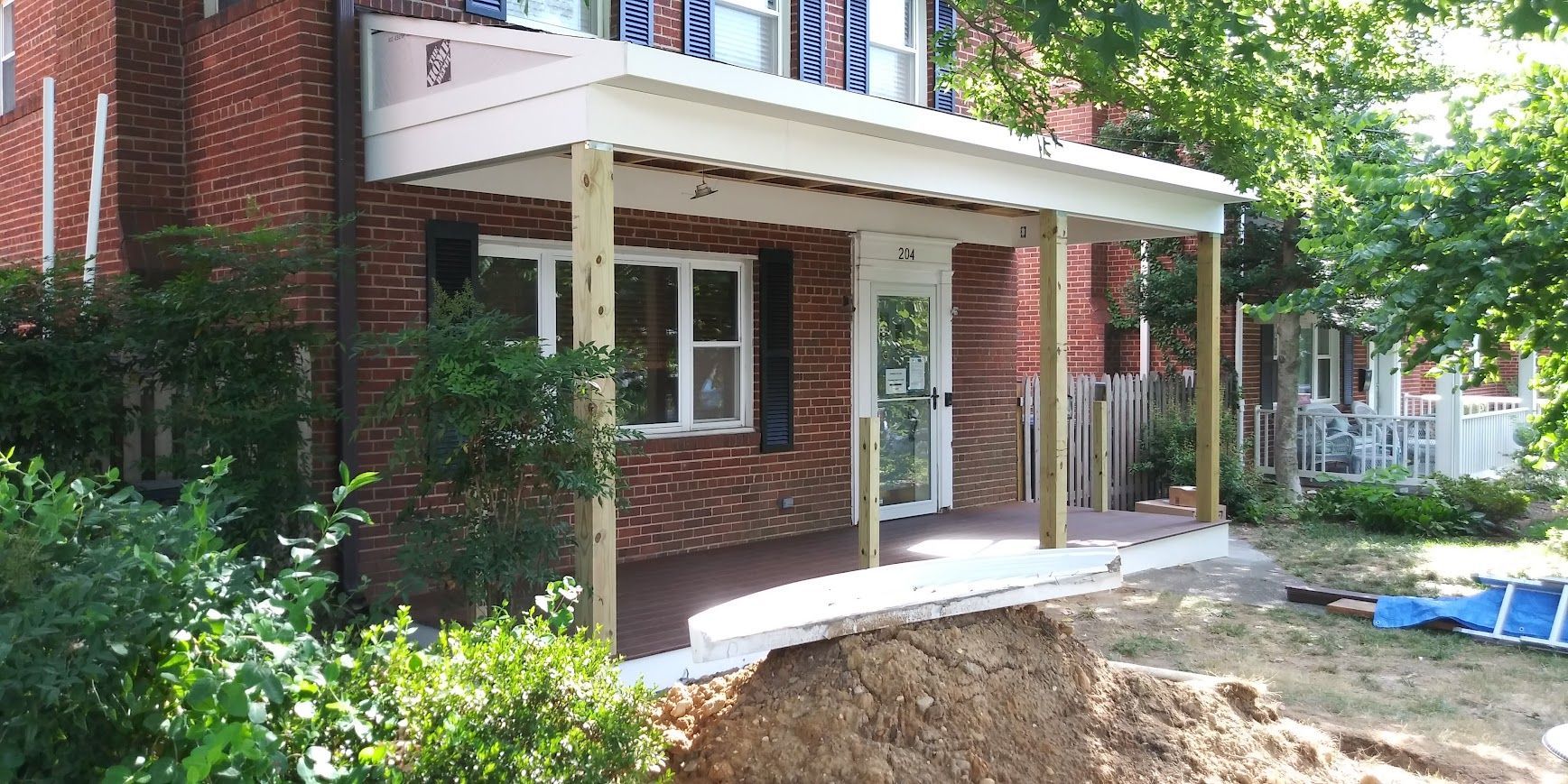 A brick house with a white porch. Unfinished dirt area in front.