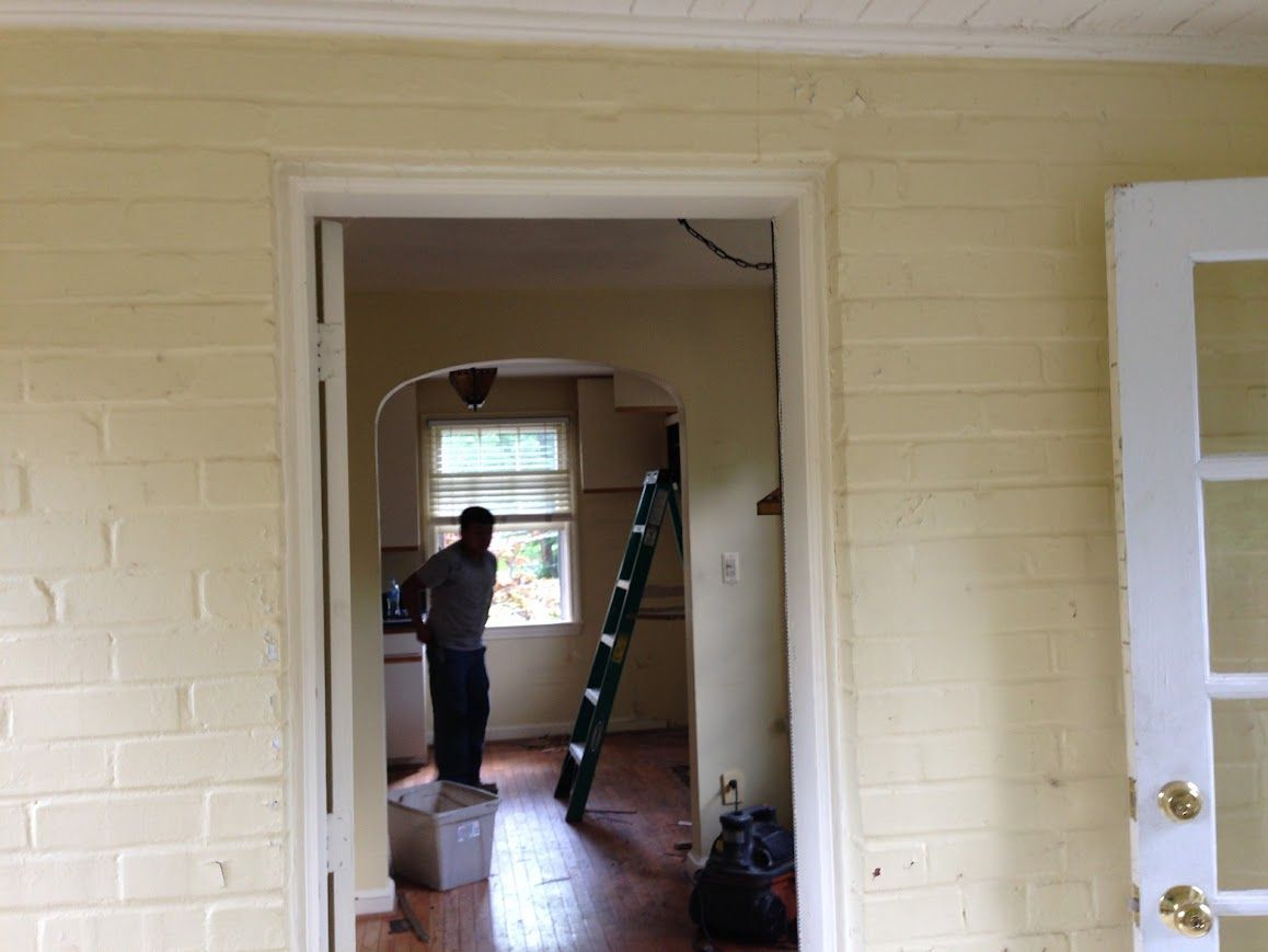 Doorway view with person in a room, light yellow painted brick walls, white trim, ladder.