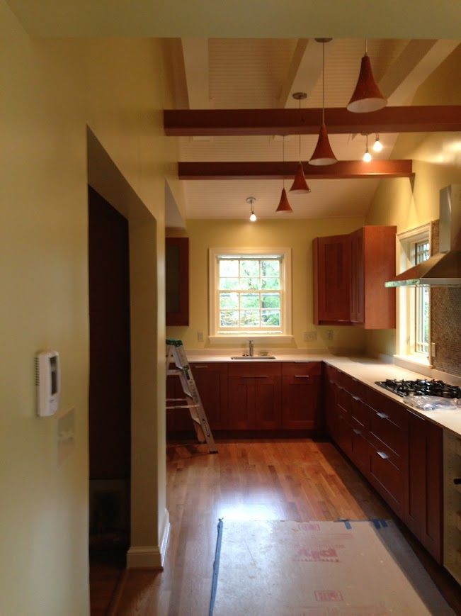 Kitchen with wood cabinets, light fixtures, and beams. Light yellow walls, hardwood floors.