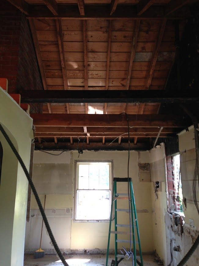 Interior view of a room under renovation, exposed ceiling beams, a window, and a ladder.