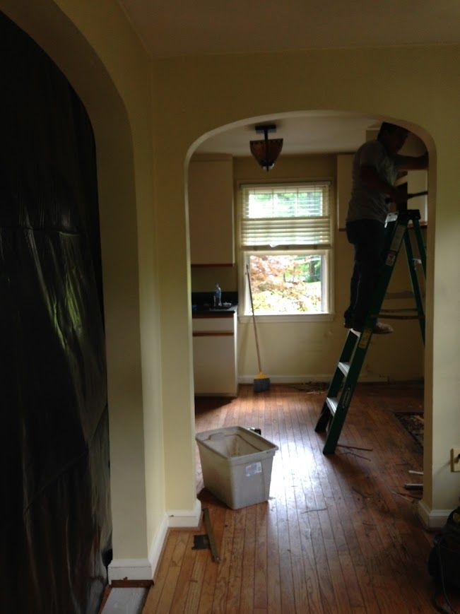A person on a ladder working on trim inside a home with an arched doorway.